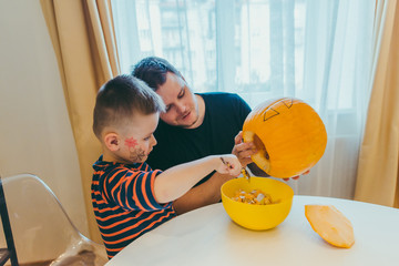 young father with toddler son making jack pumpkin head for halloween holiday