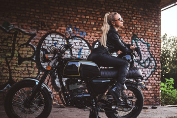 Naklejka na ściany i meble Portrait of mature attractive lady next to her vintage motorbike and graffiti brick wall.