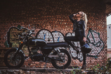 Portrait of mature attractive lady next to her vintage motorbike and graffiti brick wall.