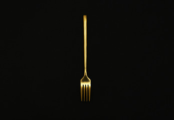 Shiny gold fork on black background, top view