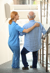 Nurse assisting elderly man on stairs indoors