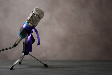 Microphone with purple awareness ribbon on table against brown background, space for text