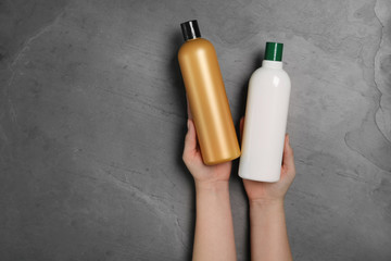 Woman holding blank bottles of cosmetic products on black background, top view. Space for design