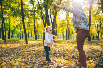 mather with little toddle daughter playing in autumn city public park