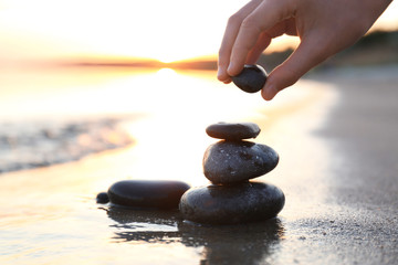 Woman stacking dark stones on sand near sea, space for text. Zen concept