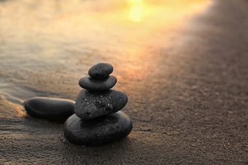 Dark stones on sand near sea at sunset, space for text. Zen concept