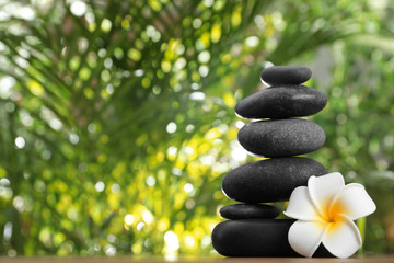 Stack of stones with flower and blurred green leaves on background, space for text. Zen concept