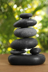 Obraz na płótnie Canvas Stack of stones on wooden table against blurred green background, closeup. Zen concept