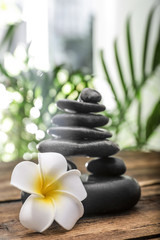 Table with stack of stones, flower and blurred green leaves on background. Zen concept