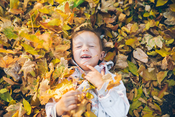 little toddler girl laying on the ground in yellow leaves
