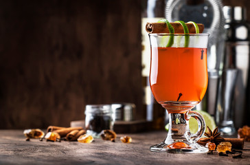 Hot rum punch, autumn or winter warming alcoholic cocktail with dark rum, port, honey, lime juice, black tea, cinnamon and cloves in tall glass on vintage wooden background
