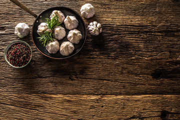 Garlic cloves and bulb with fresh rosemary in pan on old wooden table
