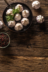 Garlic cloves and bulb with fresh rosemary in pan on old wooden table