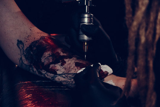 Dark toned photo of process of tattooing by experienced master.