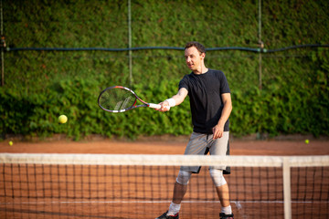 Young man playing and enjoying tennis on the clay court during lovely summer day