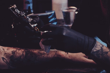 Dark toned photo of process of tattooing by experienced master.