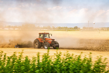 Tractor ploughing the field in sunset with dust in the air