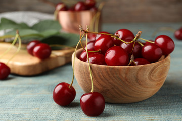 Wooden bowl of delicious cherries on blue table, closeup view. Space for text