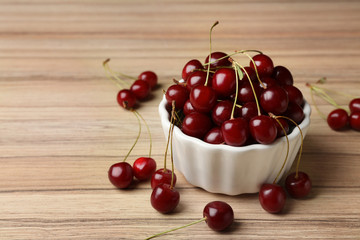 White bowl of delicious cherries on wooden table, space for text