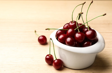 White bowl of delicious cherries on wooden table, space for text