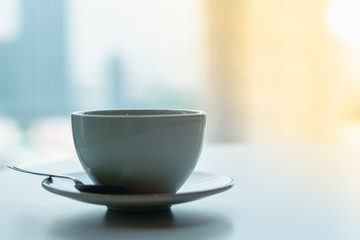 Coffee​ or tea​ cup​ blue color​ on the white​ table through the glass window of a tall building​ background, Business person's break time, Perspective of office lifestyle in big city.