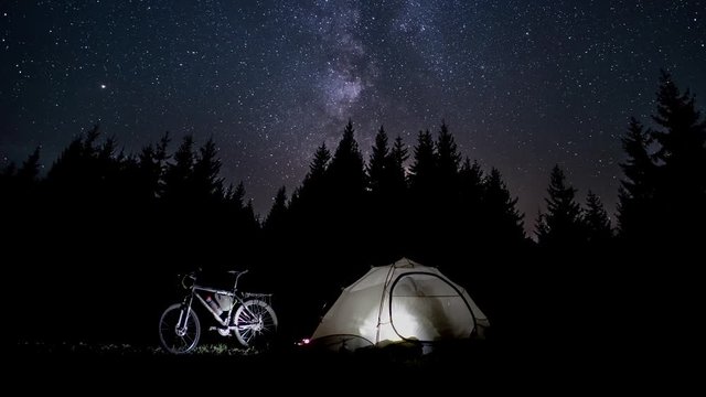 Silhouette of a man in a tent at night in night forest. The Stars and Milky Way move in the night sky. Travel concept. 4K