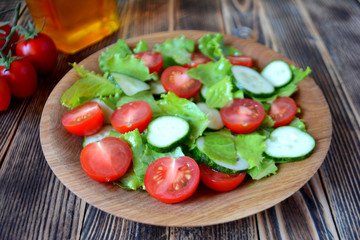 Spring or summer salad with fresh vegetables, cherry tomatoes and cucumbers in a wooden plate on a wooden background Healthy food concept