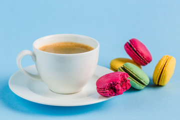 Colorful macaroons with a white Cup of coffee on a blue background, close-up, Flatley with copy space