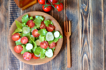 Spring or summer salad with fresh vegetables, cherry tomatoes and cucumbers in a wooden plate on a wooden background Healthy food concept