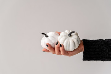 Female hand with black nails holding white and black halloween pumpkins