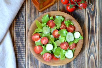 Spring or summer salad with fresh vegetables, cherry tomatoes and cucumbers in a wooden plate on a wooden background Healthy food concept