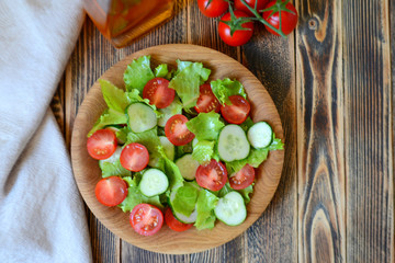 Spring or summer salad with fresh vegetables, cherry tomatoes and cucumbers in a wooden plate on a wooden background Healthy food concept