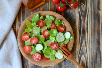 Spring or summer salad with fresh vegetables, cherry tomatoes and cucumbers in a wooden plate on a wooden background Healthy food concept