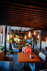 Confident young indian man in smart casual wear like orange sweater, sitting at cafe.