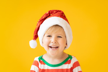 Funny child dressed Santa Claus hat against yellow background