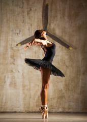 Young beautiful ballerina in black ballet tutu posing in dark studio