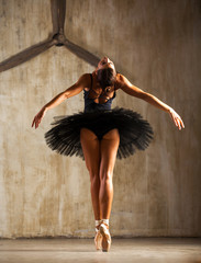 Young beautiful ballerina in black ballet tutu posing in dark studio - obrazy, fototapety, plakaty