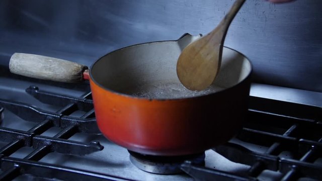 Slow motion - Chef stiring pan of boiling water on stainless steel kitchen cooker hob with wooden spoon