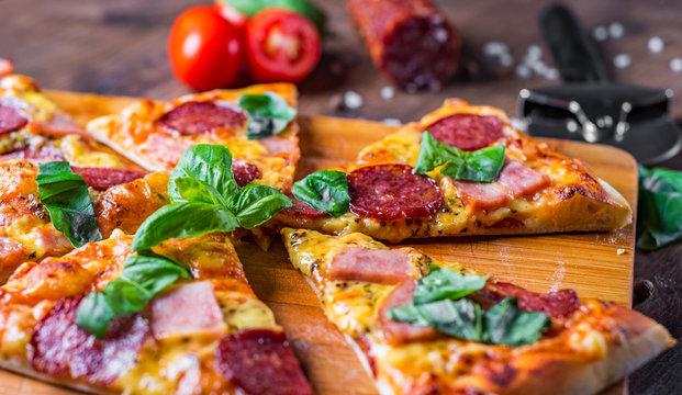 Pepperoni Pizza with Mozzarella cheese, salami, ham, Spices and Fresh basil. Italian pizza on wooden table background