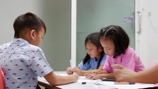 The Asian elementary school children are studying in the classroom with an Asian female teacher.