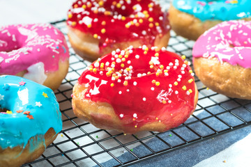 Pink and red donuts with icing and sprinkles on a baking rack