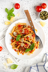 Traditional pasta putanesca with tomato sauce (capers, onions, garlic, anchovies). Tasty Italian food with Parmesan cheese, vegetarian Penne