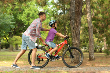 Fototapeta na wymiar Dad teaching son to ride bicycle in park
