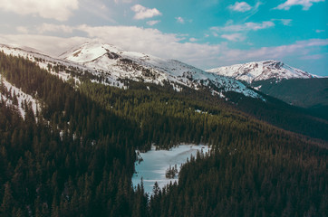 Winter carpathian mountains peaks hills with snow lake on foreground forest sunny day sky with clouds shooting on quadcopter