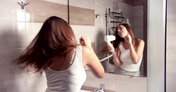 Happy young woman in top and trousers dancing with fan in bathroom having good mood, mirror reflection