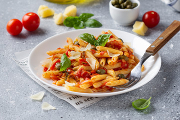Traditional pasta putanesca with tomato sauce (capers, onions, garlic, anchovies). Tasty Italian food with Parmesan cheese, vegetarian Penne