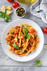 Traditional pasta putanesca with tomato sauce (capers, onions, garlic, anchovies). Tasty Italian food with Parmesan cheese, vegetarian Penne