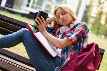 Tired female student fall asleep while  drinking coffee and studying outdoor.