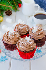 Chocolate cupcakes with cheese chocolate cream with a cup of coffee and marshmallows  for Christmas and New Year on a white wooden background.