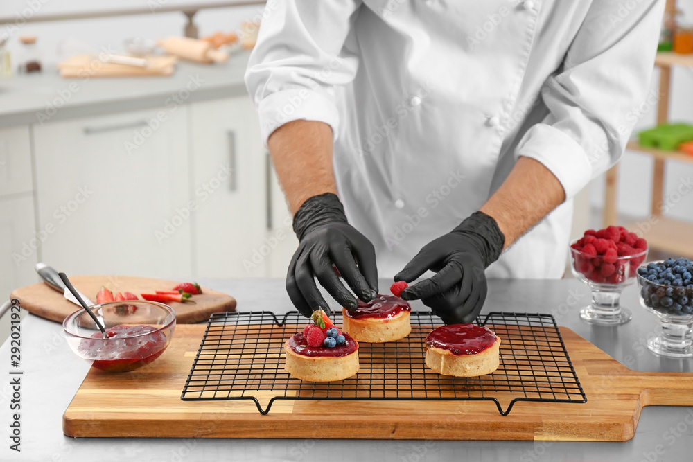 Wall mural Male pastry chef preparing desserts at table in kitchen, closeup